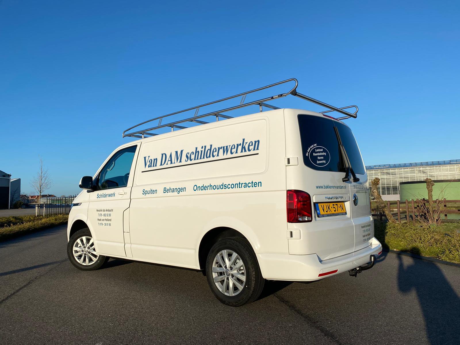 De werkbus van de schilder van Van Dam Schilderwerken. Geparkeerd op de weg. Op de achtergrond zie je wat kassen. En het is een mooie blauwe zonnige dag.